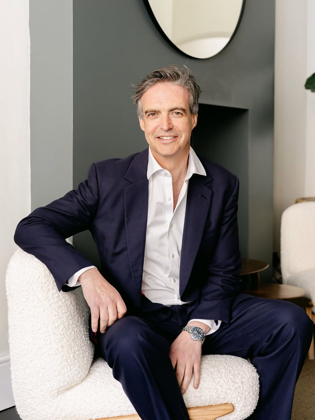 Man in a suit sitting on a white chair in a modern interior setting