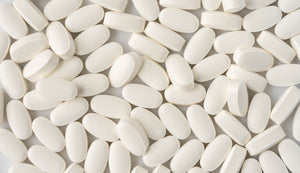 Close-up of numerous white oblong tablets scattered across a background, chondroitin and vitamin C tablets, commonly used as bone support.