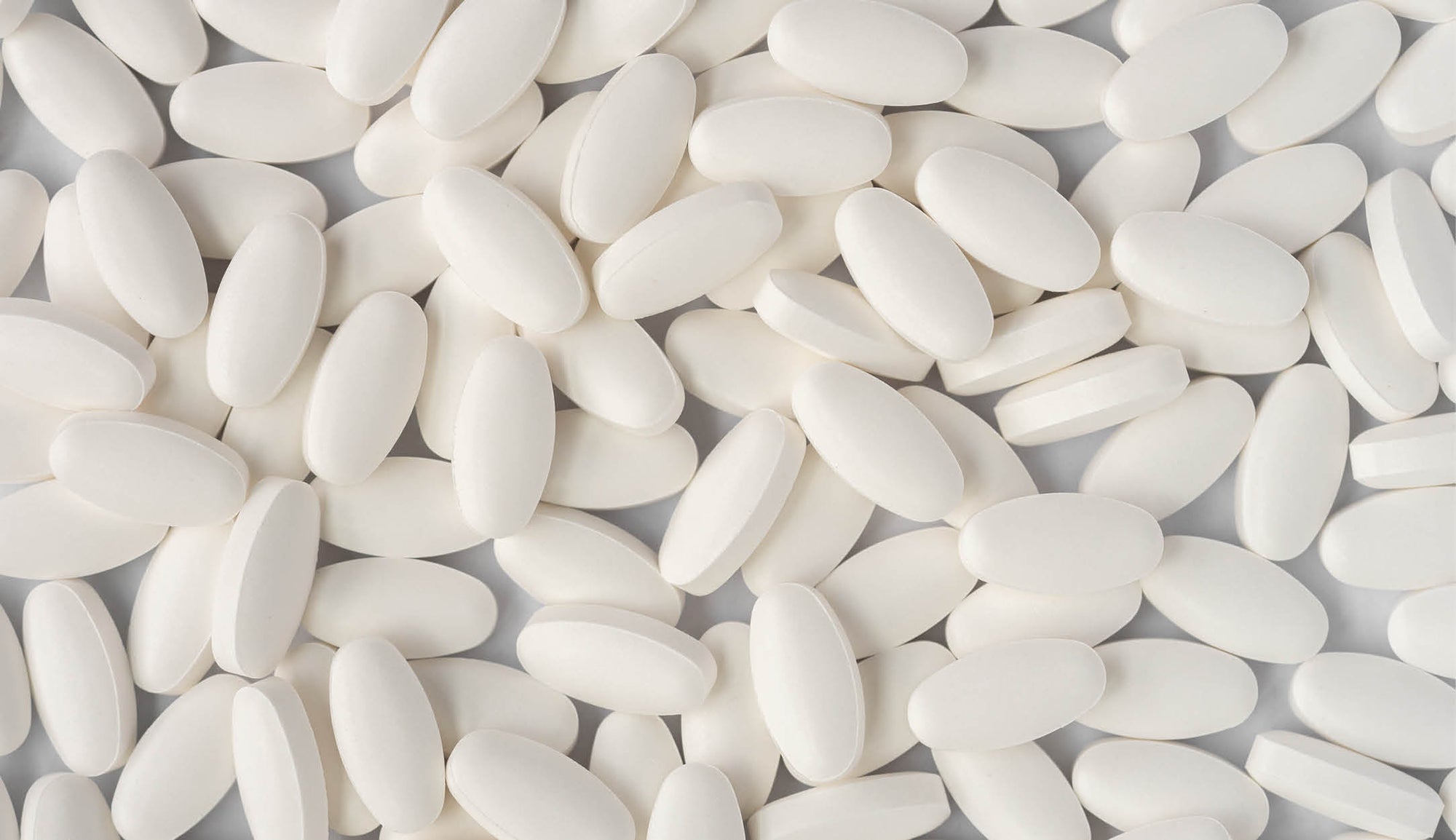 Close-up of numerous white glucosamine, chondroitin, and Vitamin C tablets scattered across a light background, highlighting the pill's smooth texture and oblong shape.