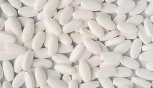 Close-up of numerous white glucosamine, chondroitin, and Vitamin C tablets scattered across a light background, highlighting the pill's smooth texture and oblong shape.
