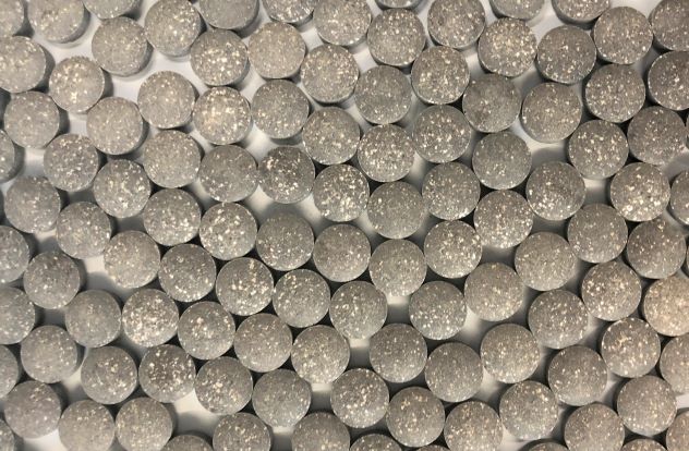 Uniformly distributed iron-zinc complex tablets with a textured surface, the metallic grey color indicative of the mineral content.