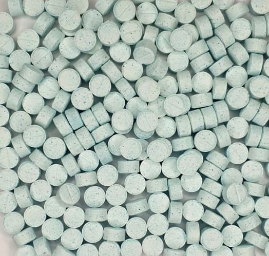 Close-up view of numerous speckled blue-green copper tablets, densely packed to display the natural supplement's texture and form, commonly used for its health benefits.