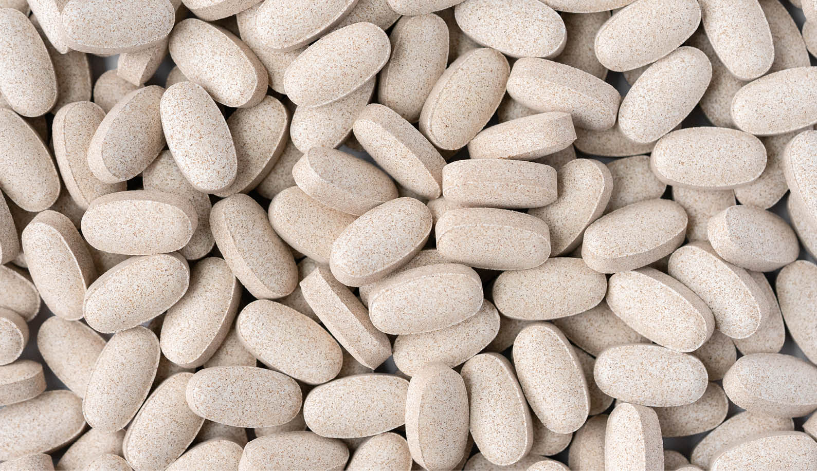Detailed image of a multitude of beige cordyceps mushroom supplement tablets clustered together, showcasing the uniform shape and natural color variation indicative of the supplement's organic origin, commonly sought for immune support.