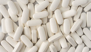 Pile of white, oblong L-glutamine tablets closely grouped together, showcasing the supplement's uniformity and matte texture.