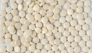 Scattered speckled tablets of an antioxidant booster supplement rich in vitamins A, C, and E, displayed as a health and wellness product.