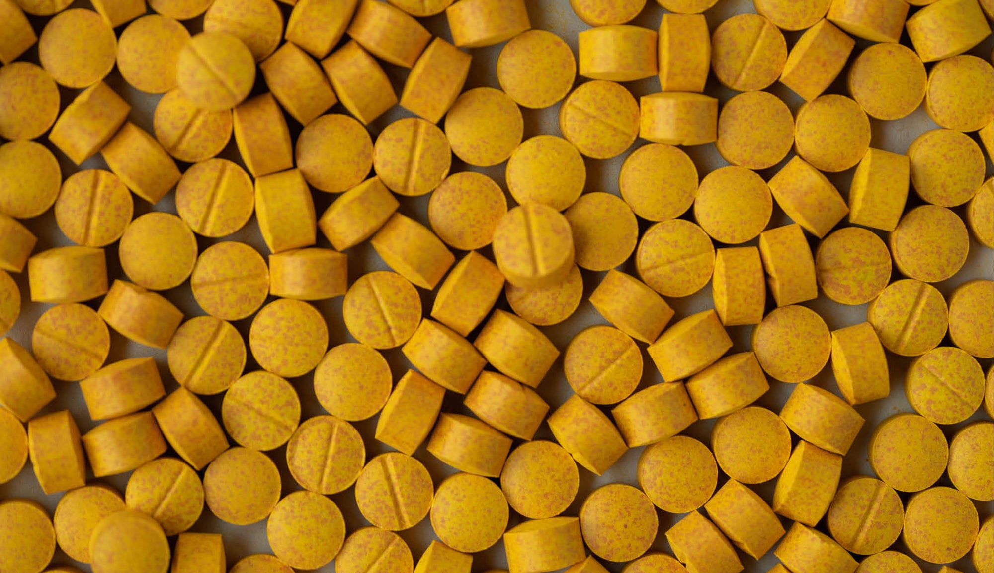 Image of densely scattered yellow turmeric tablets, with visible flecks indicating the natural composition, commonly used for their curcumin content, supportive of joint health and well-being.