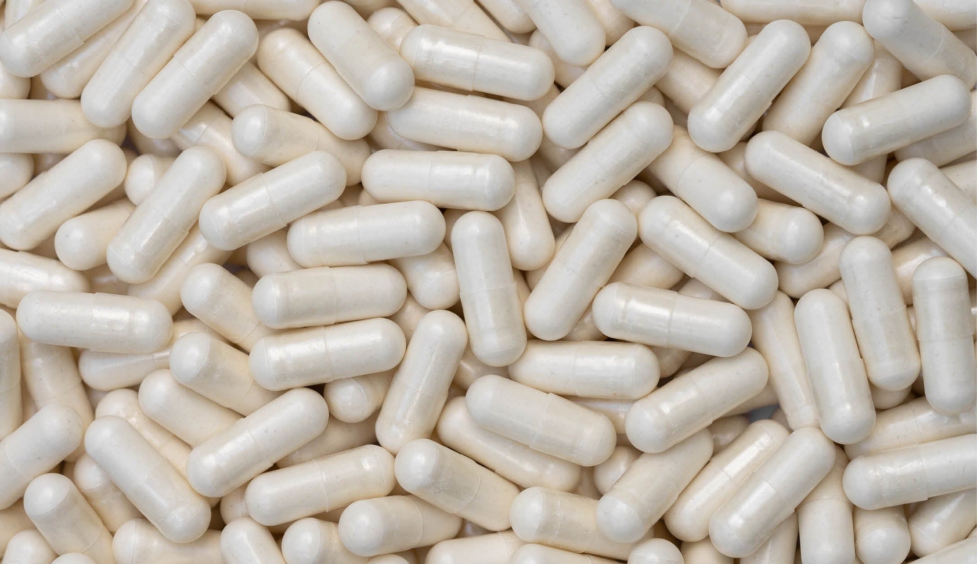 Dense array of off-white DIM (Diindolylmethane) supplement capsules with a smooth finish, randomly scattered, highlighting the consistency in size and shape, intended for supporting hormonal balance and metabolic health.
