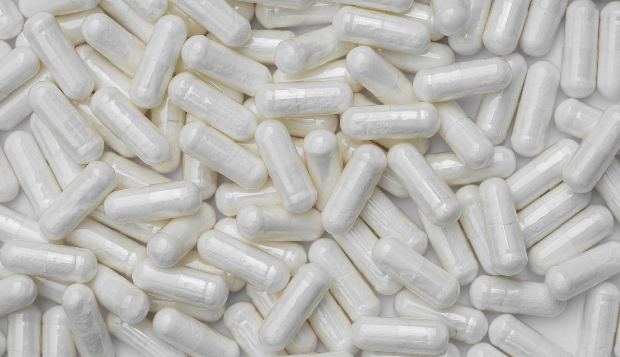 Close-up of numerous white L-carnitine supplement capsules scattered on a white surface, representing dietary supplements and health products.