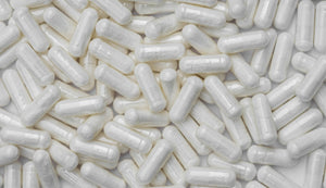 Close-up of numerous white L-carnitine supplement capsules scattered on a white surface, representing dietary supplements and health products.