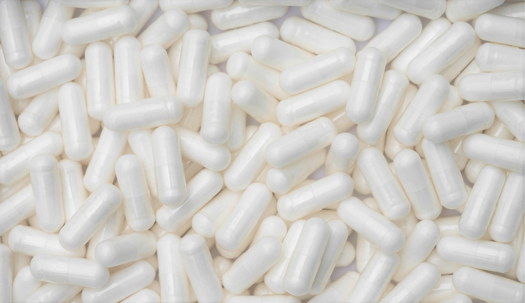 Massive collection of smooth, white L-theanine capsules heaped together.