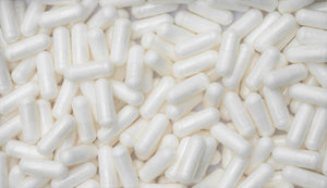 Massive collection of smooth, white L-theanine capsules heaped together.