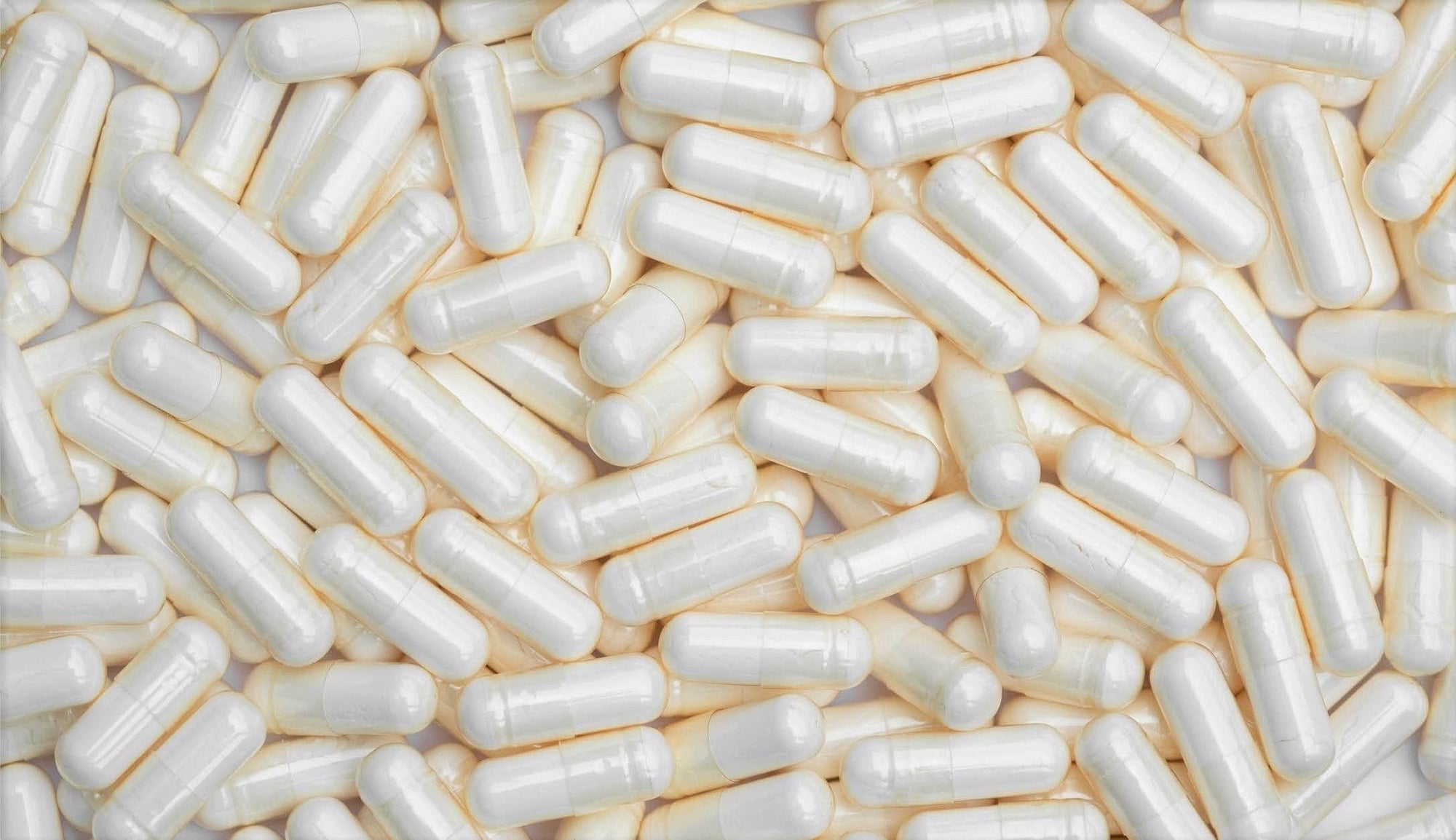 A dense spread of Lactobacillus fermentum probiotic capsules with a pearly sheen, overlapping one another to display their uniform capsule form.
